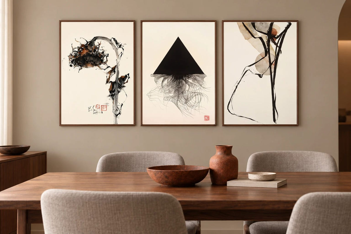 Three abstract prints hang above a wood dining table in a warm gray-beige room.