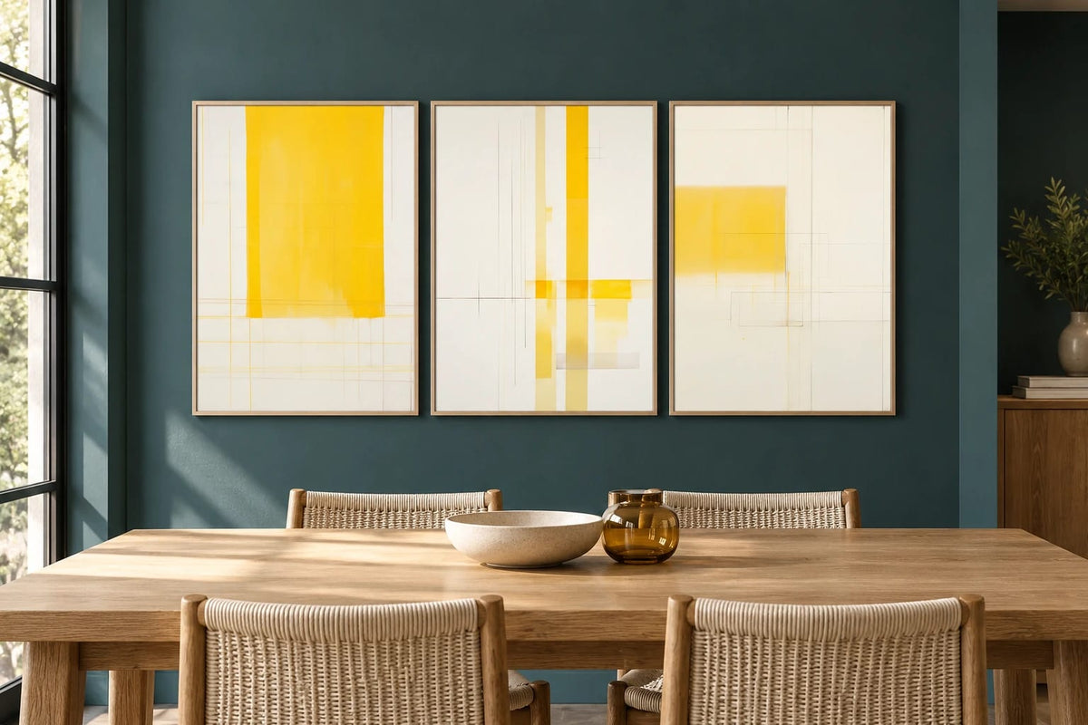 Three yellow geometric prints hang on a dark teal wall in a dining room.