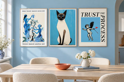Blue botanical, cat, and cherub prints hang over a table in a light dining room.