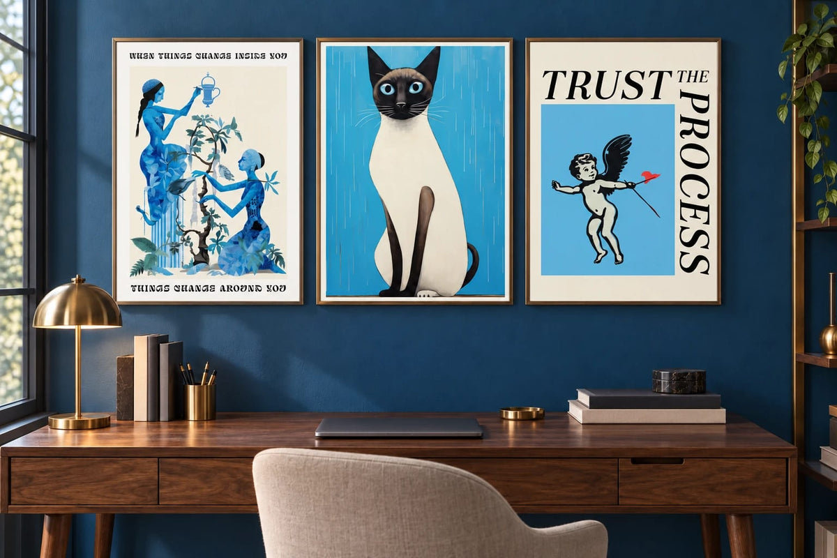 Blue botanical, cat, and cherub prints appear in an office with a dark-blue wall.